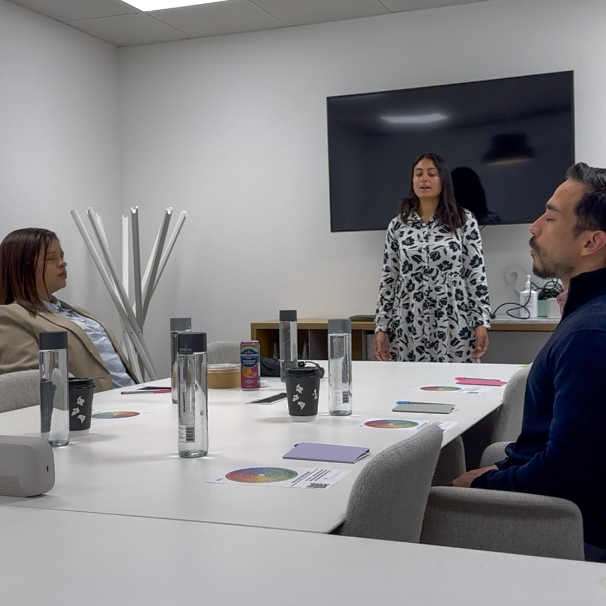 Colleagues sitting around a meeting table with eyes closed during a guided mindfulness exercise